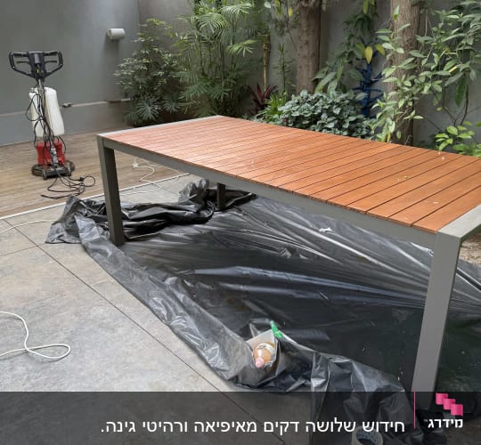 שולחן עץ עם כיסוי פלסטיק וכלי עבודה בגינה